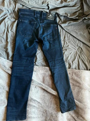 Mörkblå jeans från Replay - Snygga mörkblå jeans från Replay med raka ben och klassisk femficksmodell. Jeansen har en diskret logga på bakfickan och ett svart Replay-märke i midjan. Tillverkade i mjukt denimtyg som sitter skönt.