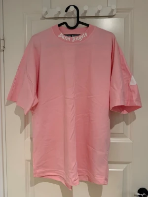 Rosa Palm Angels oversized t-shirt - Storlek S,  Säljer en rosa oversized t-shirt från Palm Angels med stort vitt logotryck på ryggen och mindre logga i halsen. T-shirten har rund halsringning och korta ärmar. Tillverkad i mjuk bomull för en skön och avslappnad look.