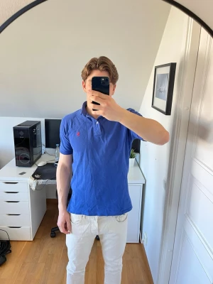 Blå pikétröja från Ralph Lauren - Klassisk blå pikétröja från Ralph Lauren med röd broderad logga på bröstet. Det är små hål i midjan (se bild 6). Hör gärna av dig vid frågor!