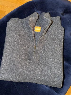 Grå stickad tröja från BOSS - Mysig grå stickad tröja från BOSS med halv dragkedja och hög krage. Tröjan har en melerad look och är perfekt för kalla dagar. Klassisk och enkel design som passar till det mesta.