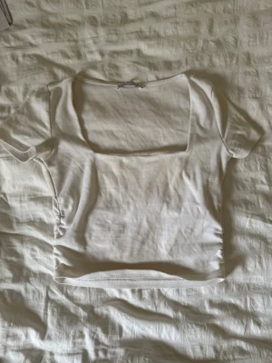 Vit croppad topp från Zara - Säljer en vit croppad topp från Zara med fyrkantig ringning och korta ärmar. Toppen är i mjuk bomull och har en enkel, stilren design som passar perfekt till jeans eller kjol. Supersnygg och enkel att matcha till olika outfits!