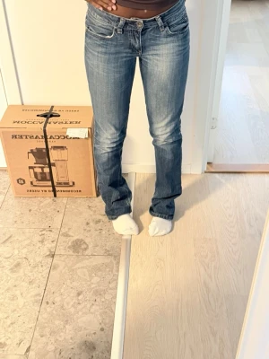 Blå bootcut jeans med låg midja - Snygga blå bootcut jeans med låg midja och klassiska fem fickor. Jeansen har en lätt tvättad look och sitter tajt över låren för att sedan bli vidare nedtill. Perfekta för en avslappnad och trendig stil.