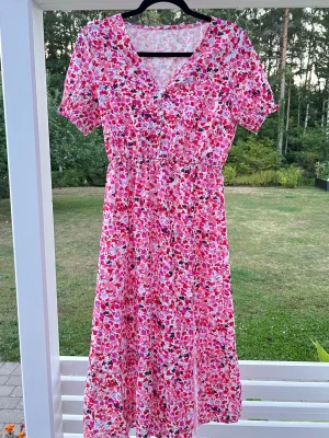 Blommig rosa långklänning med slits - Söt långklänning med blommigt mönster i rosa, rött och vitt med  v-ringning markerad midja och en liten slits. Så gullig! Mycke bra skick.
