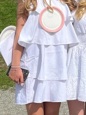 Vit klänning med volanger - Snygg vit kortklänning med omlottdesign och volangdetaljer. Klänningen har en axelbandslös look på ena sidan och ett smalt axelband på andra sidan för en asymmetrisk vibe. Perfekt för sommarens alla tillfällen. Endast använd två gånger💕