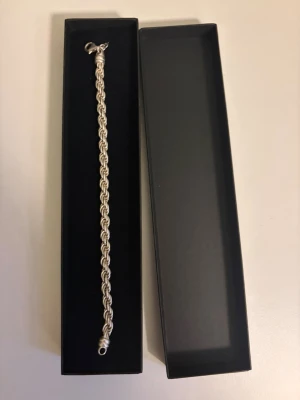 Silverfärgat kedjearmband - Snyggt silverfärgat armband med tvinnad kedjedesign. Armbandet har en klassisk karbinhake och kommer i en stilren svart ask. Perfekt accessoar för dig som gillar stilrena och tidlösa smycken. Sprillans ny 