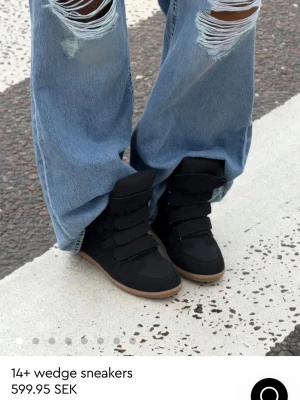 Svarta wedge sneakers med kardborre - Stilrena svarta wedge sneakers från 14+ med högt skaft och tre breda kardborreband. Skorna har en diskret kilklack och en ljusbrun sula som kontrast. Perfekta för dig som vill ha både höjd och streetstyle.