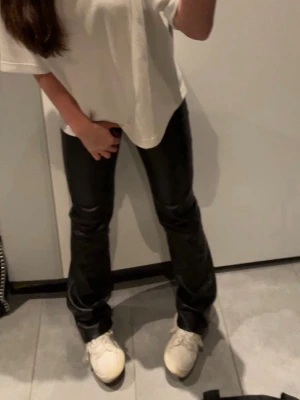 Svarta skinnbyxor - Säljer ett par svarta skinnbyxor med utsvängda ben och hög midja. Byxorna har en snygg glansig finish och sitter tight över låren för en trendig look. Perfekta för dig som vill ha ett edgy tillskott i garderoben.