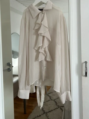Vit blus med volang och knytband - Stilren vit blus med stora volanger framtill och knytband i midjan. Jättefin till middag och sommaren, ganska tunt tyg. 