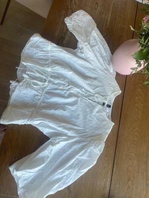 Vit blus med knytband och struktur - Säljer en vit blus med lång ärm och snygg struktur i tyget. Blusen har knytband i midjan och vid halsen för en justerbar passform. Materialet är lätt och luftigt, perfekt för en trendig look. Passar till både jeans och kjol.