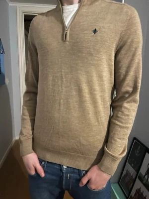 Beige stickad tröja med halvzip från Morris - Snygg beige stickad tröja med halvzip och liten broderad logga på bröstet. Tröjan har ribbade muddar vid ärmslut och nederkant samt en klassisk passform. Perfekt till jeans för en avslappnad men stilren look. Pris kan diskuteras, hör av er vid frågor! Nypris 1899kr.