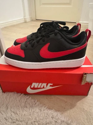 Nike sneakers låga - Snygga låga sneakers från Nike i svart och rött med klassisk vit sula. Skorna har svart ovandel i läder med röda detaljer och Nike swoosh på sidan. Perfekta för dig som vill ha en stilren och sportig look. Skön passform och tidlös design. Helt nya i din förpackning. Aldrig använda. Unisex. 