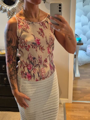 Blommig ribbad linnetopp - Säljer en söt linnetopp med ribbad struktur och blommigt mönster i rosa och rött på beige botten. Figurnära, tunt och stretchigt material. Aldrig använd. Storlek XS 