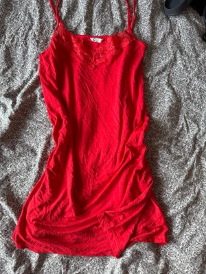 Rött nattlinne med spetsdetalj - Snyggt rött nattlinne med tunna axelband och spetsdetalj vid urringningen. Mjukt och lätt material som känns skönt mot huden. Perfekt för mysiga kvällar hemma.