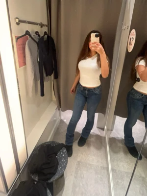 Blå bootcut jeans med låg midja - Säljer ett par klassiska blå bootcut jeans med normal midja och smal passform upptill som går ut lite vid bensluten. Jeansen har fem fickor och stängs med dragkedja och knapp. Perfekta till en enkel t-shirt eller hoodie. Dock lite trasiga