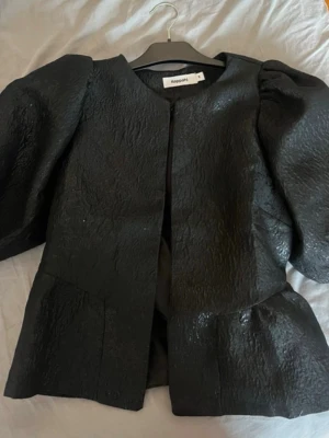 Svart puffärmad blus från Kappahl - Trendig svart blus från Kappahl med puffiga axlar och struktur i materialet. Blusen har rund halsringning och är tillverkad i ett glansigt tyg som ger en cool look. Perfekt för dig som vill sticka ut med en statement-blus.