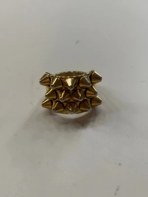 Guldig ring med nitar - Peak Ring i guld med tre rader av spetsiga nitar runt hela ringen. Ringen har en chunky och edgy design som verkligen sticker ut och passar perfekt för dig som gillar statement-smycken. Ringen är från Edblad.