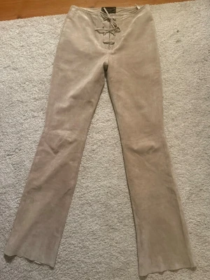 Beige mocka byxor med snörning - Snygga beige mockabyxor från  tomahawk med snörning framtill i midjan. Byxorna har utsvängda ben och är i 100% äkta mocka i storlek 36