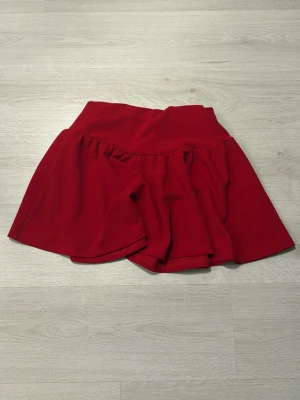 Röd volangkjol - En röd kortkjol med volang och bred midja. Kjolen har en enkel, flowy form. Perfekt för dig som gillar färgstarka plagg och vill ha något bekvämt och stilrent. Använd 1 gång