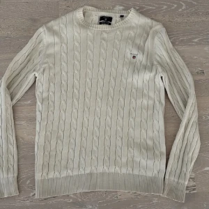 Vit kabelstickad tröja från Gant - Kabelstickad tröja i vitt från Gant med rund halsringning och ribbade muddar. Tröjan har Gant-logga broderad på bröstet och är gjord i premium bomull. Perfekt för dig som gillar klassisk och stilren look.