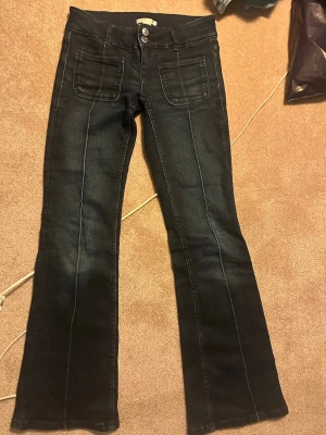 Mörkblå low waist bootcut jeans - Säljer ett par mörkblå bootcut jeans från Gina Tricot med raka ben och markerade sömmar framtill. Jeansen har två stora framfickor och dubbla knappar i midjan. Perfekta för en avslappnad men ändå trendig look.