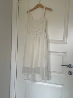 Vit somrig klänning - Luftig vit klänning med smala axelband och lätt rynkad överdel. Kjolen är något längre bak och har ett tunt, svepande tyg som ger en flowy känsla. Använd 1 gång. Orginal pris: 399kr