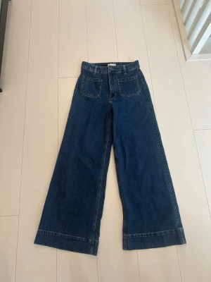 Blåa wide leg jeans med fickor fram - Säljer ett par mörkblå wide leg jeans med raka, vida ben och stora framfickor. Jeansen har hög midja och klassisk denimlook, perfekta för en avslappnad och trendig stil. Materialet är kraftig bomullsdenim. HM.