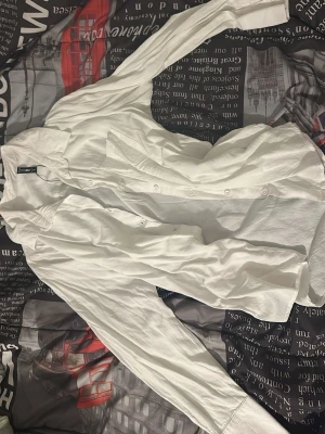 Vit klassisk skjorta från H&M - Säljer en vit långärmad skjorta från H&M med klassisk krage och knäppning framtill. Skjortan har en rak passform och är tillverkad i ett lätt bomullstyg som passar perfekt till många olika stilar.
