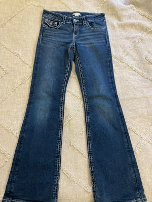 Blå bootcut jeans med kontrastsömmar - Mörkblå bootcut jeans med snygga kontrastsömmar från Gina young. Jeansen har utsvängda ben och dekorativa ficklock bak. Perfekta för en avslappnad och trendig look. Storlek 158.