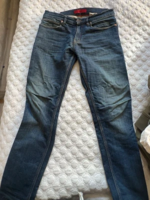 Blå slim fit jeans med tvättade detaljer - Säljer ett par blå slim fit jeans med snygga tvättade detaljer och klassisk femficksmodell. Jeansen har normal midja och raka ben. Materialet är denim i bomull med lite stretch för extra komfort. Perfekta för en avslappnad och trendig stil.