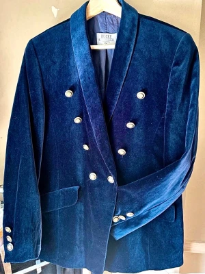 Vintage Hucke Mode Collection International blå sammets kavaj - Snygg mörkblå sammetskavaj från Hucke med dubbelknäppning och guldfärgade knappar. Klassisk modell med breda slag och fickor framtill. Perfekt för dig som vill sticka ut med en elegant och trendig look.  Bystmått - ca 50cm Armlängd - ca 59cm Längd - ca 67cm