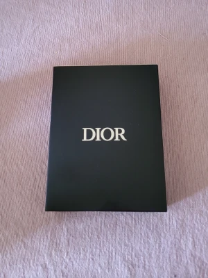 Dior läppkit med tre produkter - Snyggt läppkit från Dior med tre produkter i exklusiv svart ask. Innehåller ett ljusrosa läppglans, ett rosa Lip Glow Color Reviver Balm och ett nude/brunt flytande läppstift. Lyxig design med silverdetaljer och genomskinliga hylsor.