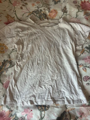 Vit basic t-shirt i bomull - En enkel vit t-shirt i mjuk bomull med rund hals och korta ärmar. Perfekt att matcha med jeans eller kjol för en clean och avslappnad look. Fint skick bara att man kan stryka den lite