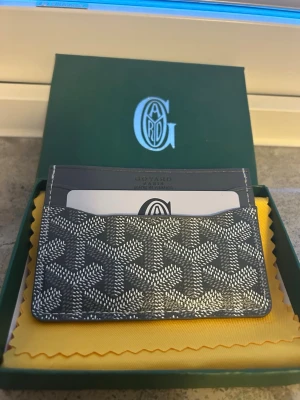 Grå korthållare - Snyggt svart kortfodral med det klassiska vita mönstret och flera kortfack. Tillverkad i canvas och läder, perfekt för att hålla koll på dina kort. Kommer i originalask med gul putsduk.