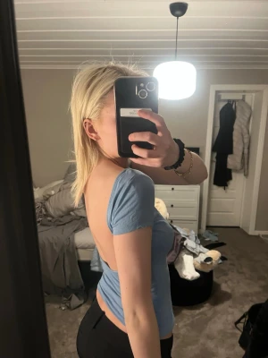 Ljusblå croppad topp med öppen rygg - Trendig ljusblå croppad topp med korta ärmar och snygg öppen rygg. T-shirten har en tight passform och är tillverkad i mjukt bomullsmaterial. Perfekt för dig som vill ha en enkel men ändå iögonfallande topp.