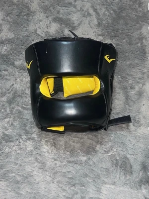 Svart och gul boxningshjälm Everlast - Säljer hjälmen då för att den inte har använts på länge.   Produkterna är använda men i ett fullt fungerande och bra skick.    -Boxningshjälm (Everlast): Svart med gul insida, storlek M/L. Kvalitetshjälm från ett toppläge (nypris ca 850 kr). ! Få ett gratis hopprep tillsammans 