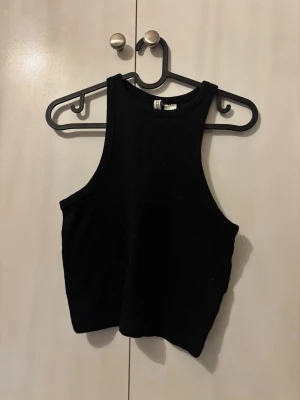 Svart croppad linnetopp - Snygg svart croppad linnetopp med hög hals och ärmlös design. Perfekt att matcha med höga jeans eller kjol för en trendig look. Tillverkad i mjukt bomullsmaterial som känns skönt mot huden.