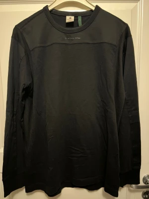 Svart långärmad tröja G-Star Raw - Stilren svart långärmad tröja från G-Star Raw med rund halsringning och diskret logga framtill. Tillverkad i mjukt bomullsmaterial som känns skönt mot huden. Perfekt till ett avslappnat streetwear-utseende.