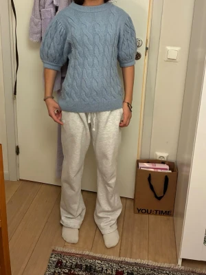 Ljusblå stickad tröja med kort ärm - Ljusblå stickad tröja med kabelstickat mönster och korta puffärmar. Tröjan har rund halsringning och en loose passform som är både chill och snygg. Perfekt att matcha med jeans eller mjukisbyxor för en avslappnad look.