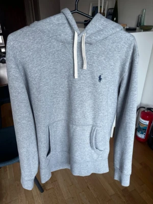 Grå Hoodie från Polo Ralph Lauren - Snygg grå hoodie från Polo Ralph Lauren med klassisk huva och vita dragsnören. Storlek S. Mycket bra skick! Kvitto går att lösa!