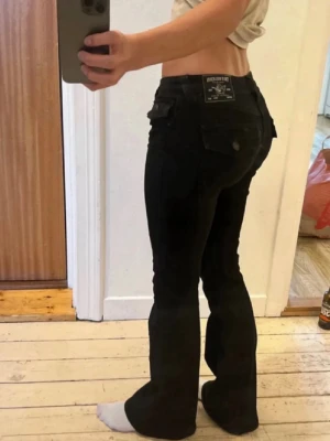 Svara true religion low waist - Säljer ett par svarta bootcut jeans från true religion med låg midja och klassiska bakfickor med lock. Jeansen har en snygg passform som sitter tight upptill och släpper ut vid benen. Materialet är stretchigt och bekvämt, perfekt för en trendig look. Dem är midwaist