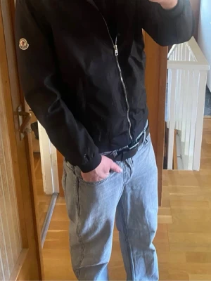 Moncler jacka s/m - Snygg svart jacka från Moncler med klassisk logotyp på ärmen och hel dragkedja framtill. Jackan har en stilren design med ribbade muddar och två sidofickor. Perfekt för dig som vill ha en enkel men exklusiv look. Inga skador eller slitelser nånstans och nfc funkar.