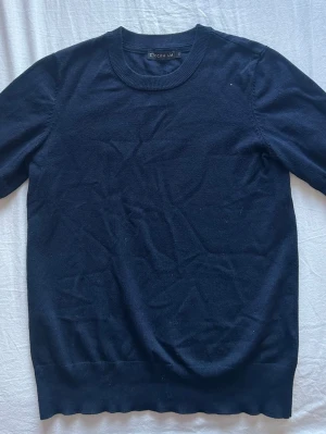 Mörkblå stickad tröja STOCKH LM - Kortärmad stickad mörkblå tröja. Tröjan har rund halsringning, ribbade muddar och är ett mjukt stickat material. Perfekt basplagg för lager på lager och funkar året runt. Den är i storlek xs och bara använd några få gånger!