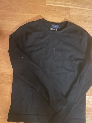 Svart stickad tröja från Riley - Klassisk svart stickad tröja från Riley i mjuk merinoull. Tröjan har rund halsringning och långa ärmar, perfekt för lager på lager. Enkel och stilren design som passar till det mesta.