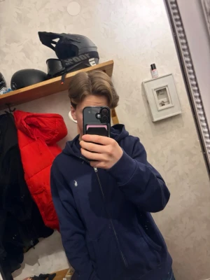Mörkblå hoodie från Polo Ralph Lauren - Säljer en mörkblå hoodie från Polo Ralph Lauren med dragkedja och huva. Klassisk liten vit logga på bröstet och två fickor framtill. Perfekt för dig som gillar stilren och enkel design. Inga defekter och endast använd fåtal gånger. Original pris ~1200. Priset är inte hugget i sten. Skriv om ni undrar något!
