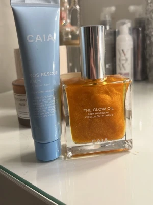 CAIA SOS Rescue Balm & Glow Oil - Säljer ett kit med CAIA SOS Rescue Balm i blå tub och The Glow Oil i fyrkantig glasflaska med silvrig kork. Balmet är återfuktande och oljan ger en skimrande finish med avokadoolja och vitamin E. Perfekt för dig som vill boosta glowet.