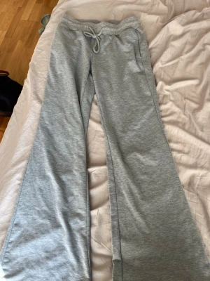 Gråa utsvängda mjukisbyxor - Säljer ett par gråa mjukisbyxor med utsvängda ben och dragsko i midjan. Byxorna har fickor på sidorna och är gjorda i mjukt sweatshirtmaterial, perfekta för chill dagar. Inget synligt märke.
