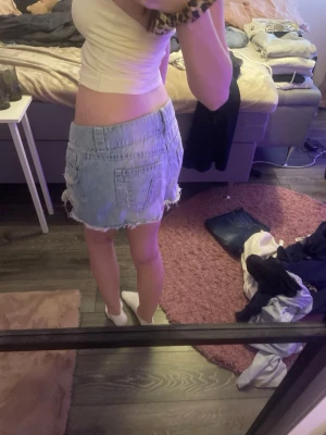 Ljusblå jeanskjol med fransad kant - Säljer en ljusblå jeanskjol med fransad, rå kant och slitna detaljer. Kjolen har klassiska fickor fram och bak, köpt på Gina Young.