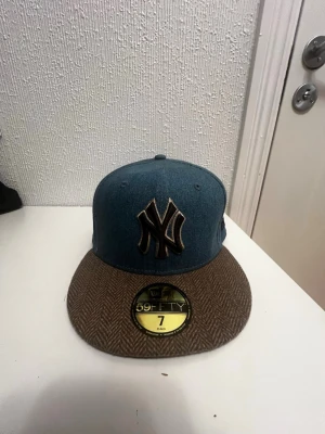 New Era Yankees keps blå/brun - Snygg New Era 59FIFTY keps med New York Yankees-logga i svart och guld framtill. Kepsen har blått tyg på kronan och ett brunt, fiskbensmönstrat tyg på skärmen. Broderad MLB-logga baktill. Perfekt för dig som vill sticka ut med stilren streetwear.