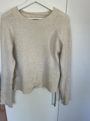 Beige stickad tröja med rund hals - Mysig beige stickad tröja med rund halsringning och långa ärmar. Tröjan har ribbade muddar vid ärmslut och nederkant, vilket ger en klassisk och enkel look. Perfekt att matcha med jeans eller kjol för en avslappnad stil.