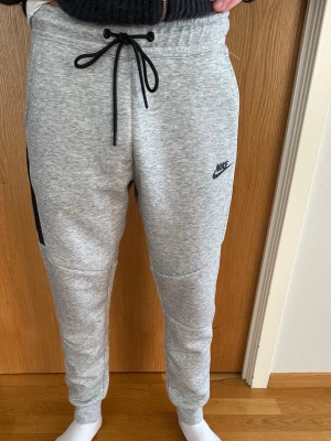 Grå Nike tech byxor  - Hej! Säljer min fina Nike tech byxor då den blivit för liten på mig. Referens: 186 cm & 70 kg. Superfint skick, inga defekter eller liknade, som ny! Passar till vardagen, träning eller varför inte hemma. Nypris är cirka 1200. Kvaliten är oslagbar och byxorna är väldigt eftertraktade. Vid fler frågor eller funderingar, hör gärna av er i dm! Väl mött, Arvid😁🙌